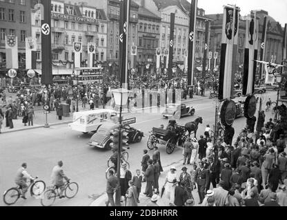 'The photograph shows the street Unter den Linden in Berlin at the level of Friedrichstrasse around the time of the 1936 Summer Olympics. Passers-by crowd on the sidewalks, in the background there is a double-decker bus with the advertising slogan ''Berlin smokes Juno'' in front of the Loewenbraeu in Munich. In the street hang swastika flags and flags with different coats of arms (presumably city arms).' Stock Photo