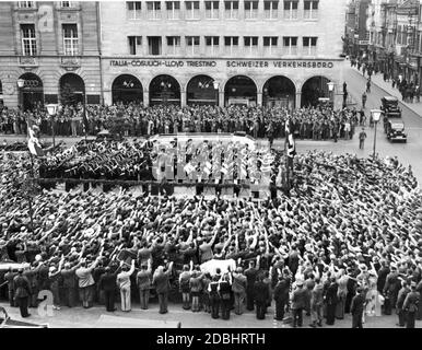 The Academia Musica of the Opera Nazionale Balilla (youth organization of the Italian fascists) plays a concert at the Kranzler-Ecke ( boulevard Unter den Linden, corner Friedrichstrasse) in Berlin in 1937. The crowd performs the Nazi salute. They stand in front of the Haus der Schweiz. On the left side there is a car dealer who sells the brands of Auto Union. Stock Photo