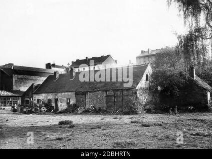 The 1932 photograph shows a decaying, abandoned old farmhouse in Berlin at Muellerstrasse 16, behind which the more modern houses and tenements of the growing city already rise up. Stock Photo