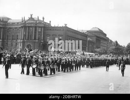 A marching band of the Reichsmarine, followed by several other sailors, crosses the street Unter den Linden in Berlin in 1933. The people at the side of the street perform the Nazi salute. In the background are the Alte Bibliothek (left), the Alte Palais (right) and the equestrian statue of Frederick the Great (right). Stock Photo