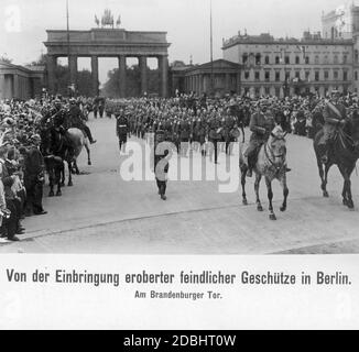 At a military parade in September 1914, enemy guns captured during the war were presented in front of the Brandenburg Gate in Berlin. The picture shows a crowd of people watching the parade of a marching band. Two officers are riding in front. Stock Photo