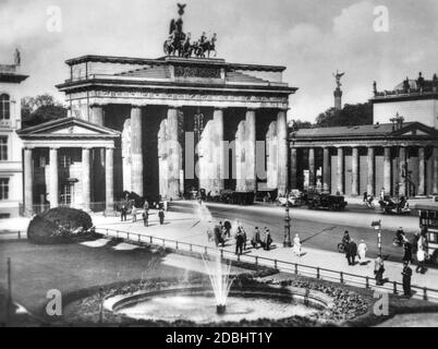 Pedestrians are walking across Pariser Platz in front of the Brandenburg Gate in Berlin. In the background on the right, the Victory Column, which at that time still stood in front of the Reichstag on Koenigsplatz (today: Platz der Republik). The picture was taken around 1920. Stock Photo
