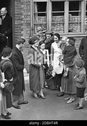King George VI (2nd from left) and Queen Elizabeth (3rd from left) visit the poorer districts in South London. Here in conversation with the residents of the McManus House in Battersea. Stock Photo