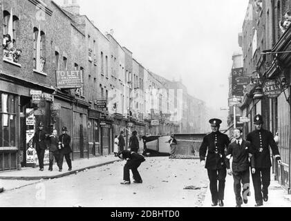 'After riots in the wake of the cancellation of a planned demonstration by the ''British Union of Fascists'' in Whitechapel, policemen led demonstrators away in London's Cable Street. In the background an overturned truck bears witness to the riots.' Stock Photo