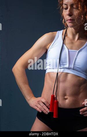 athlete girl with flawless muscles and athletic body, holding a skipping rope, posing against a textured blue wall background Beautiful sports girl do Stock Photo