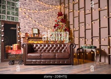 Stylish christmas decorations in brown living room with sofa, christmas tree and garlands on the wall Stock Photo