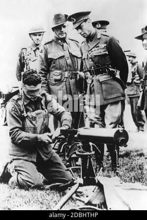 During a visit to the troops King George VI (right) watches an Australian soldier assembling his machine gun blindfolded. Stock Photo