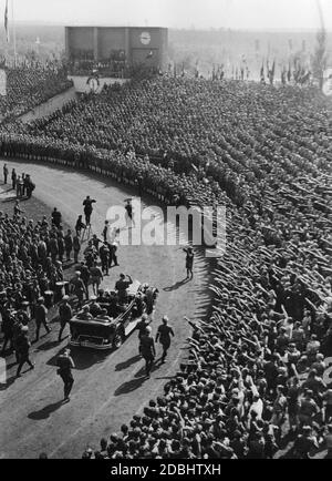 Adolf Hitler, standing in a Mercedes, drives around in the Municipal Stadium and greets the participants of the Hitler Youth at their rally during the Nazi Party Congress in Nuremberg. On the back seat on the left, Adjutant Wilhelm Brueckner, on the right, Baldur von Schirach. On the left is a drum corps of the Hitler Youth. Stock Photo