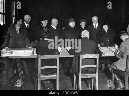 Voters take a look at the electoral rolls for the Reichstag election and the referendum on the withdrawal from the League of Nations on 12.11.1933 to check whether they are on the lists. Among the election workers there is a National Socialist. Stock Photo