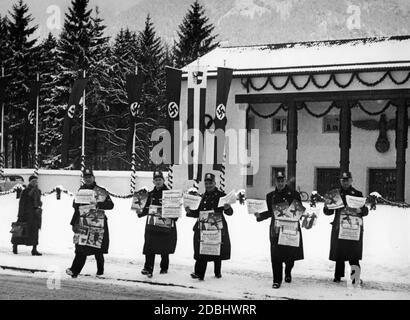 'Newspaper dealers of the Scherl publishing house with issues of the ''Lokal-Anzeiger'' in front of the Kongresshalle in Garmisch-Partenkirchen during the Winter Olympics. Between swastika flags hangs a flag with the coat of arms of Garmisch-Partenkirchen.' Stock Photo