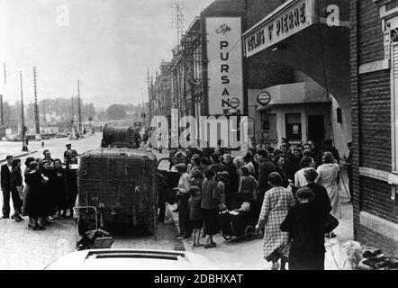 The National Socialist People's Welfare is announced in Amiens through loudspeakers. A car of the NSV is parked on a street in front of a store, where a crowd has formed. Stock Photo