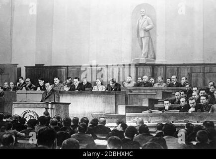 The formal head of the Soviet Union was Mikhail Kalinin, who sits left in the background at the wall with Georgy Malenkov. The speaker is the People's Commissar of Finance A. Zverev. Under the statue of Lenin, from right to left: L. Beria, V. Molotov, A. Mikejan, Y. Stalin, K. Voroshilov, N. Khrushchev, L. Kaganovich, A. Zhdanov. Behind the lectern from left to right: T. Lysenko, U.  Yusupov, A. Andreyev, N. Shvernik, Ch. Aslanova, and M. Kulagin. Stock Photo