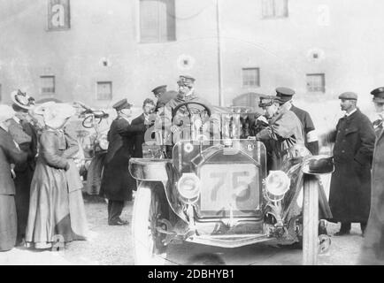 Prince Henry of Prussia (centre left) sits at the wheel of his car (a 40-horsepower Benz with number 75) during the Hercomer ride of 1906, which took place between the 6th and 12th of June. Here he makes a stop in Munich. Left of the bonnet is the logo of the Kaiserlicher Automobil-Club. Stock Photo