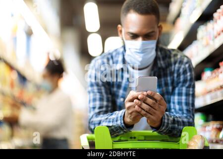 Black Man With Smartphone Shopping Food In Supermarket Wearing Mask Stock Photo