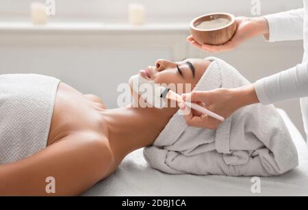 Relaxed asian woman getting facial nourishing mask by beautician at cosmetology cabinet Stock Photo