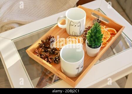 Wooden tray with white mugs, orange chips and christmas decorations on white table Stock Photo