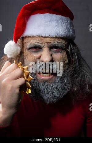smiling santa with a grin, looking at the camera, evil santa dead - mummy. Christmas horror concept Santa Claus holding copyspace blank sign. Portrait Stock Photo