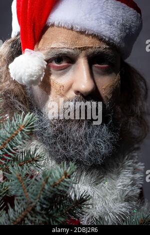make-up santa peeping out of the tree. halloween concept christmas zombie santa dead Santa Claus holding skis in his hands and gifts Stock Photo