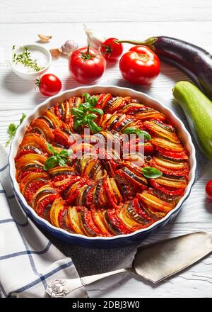 ratatouille, vegetable stew of sliced eggplant, zucchini, onion and potato with tomato sauce, ingredients at the background, french cuisine, vertical Stock Photo