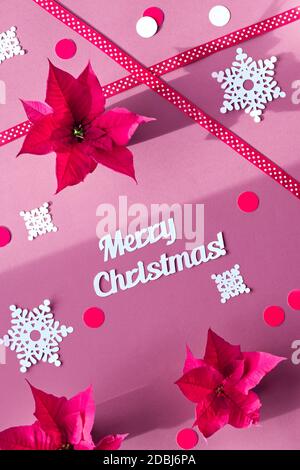 Text Merry Christmas. Poinsettia, snowflakes, dual-color paper confetti. Top view, red purple design Stock Photo