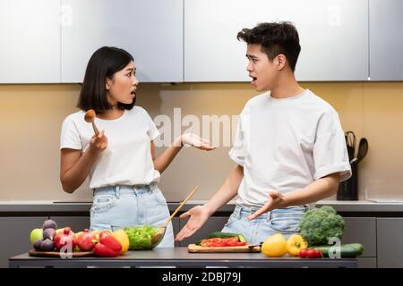 Asian Couple Having Conflict While Cooking In Kitchen At Home