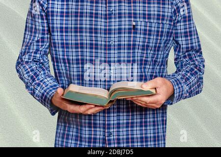 Closeup of hands from a man in a blue and white striped shirt holds an old book in his hands and reads. Businessman in front of bright stone wall. Mac Stock Photo