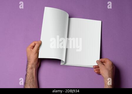 Male hands holding an opened book-catalog with blank pages on purple background, mock-up series template ready for your design, pages selection path i Stock Photo