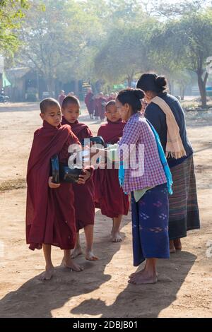 Procession of Buddhist monks collecting alms at Bagan, Myanmar (Burma), Asia in February - local women giving rice and food Stock Photo