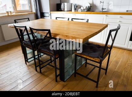 A big wooden dining table with glass blocks and metal wicker chairs and pillows in modern scandinavian an eat-in kitchen, against light wood floor, br Stock Photo