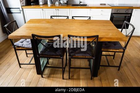 A big wooden dining table with glass blocks and metal wicker chairs and pillows in modern scandinavian an eat-in kitchen, against light wood floor, br Stock Photo
