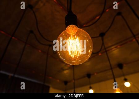 Close-up of big vintage incandescent lights bulb hanging in a dark room. Decorative edison light bulbs with straight wire. Dimmable, warm white, E27. Stock Photo