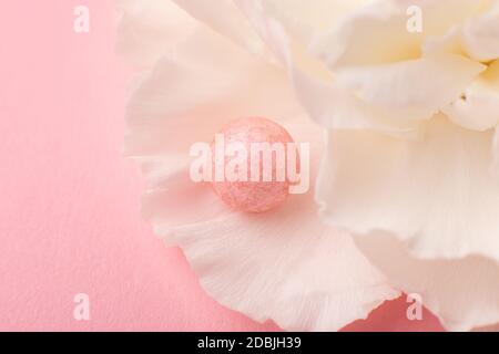 Delicate close-up shot of pink ball of pearl face powder on petals of carnation flower. Concept for articles on makeup and skin care. Stock Photo