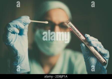 Conceptual photograph of a doctor holding and looking at a test tube while testing samples for presence of coronavirus (COVID-19). Stock Photo