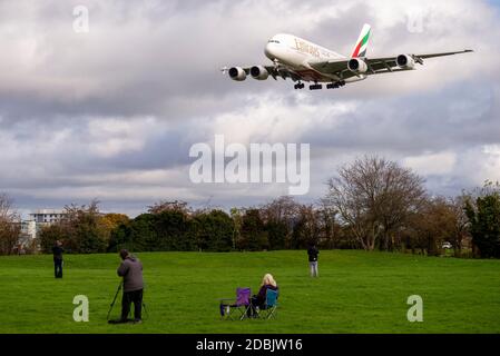 Plane spotters, aviation enthusiasts, in the green space park near Myrtle Avenue watching a jet airliner plane landing at London Heathrow Airport, UK Stock Photo