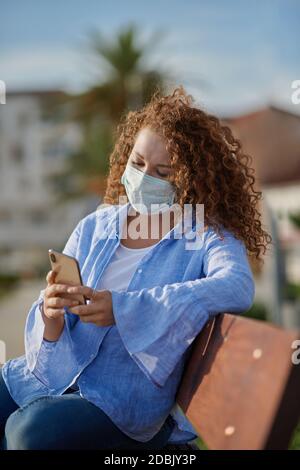 Beautiful young woman in mask using smart phone Stock Photo