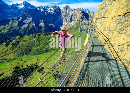 Thrill walk on Schilthorn, Bernese Prealps, Canton of Bern in Switzerland. Caucasian tourist woman walks on a net between high rock faces at mid Stock Photo