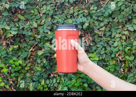 Aluminum thermos mug on hand with green leaves wall, stock photo Stock Photo