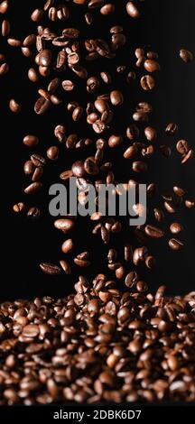 Falling coffee beans isolated on black background. Vertical photo Stock Photo