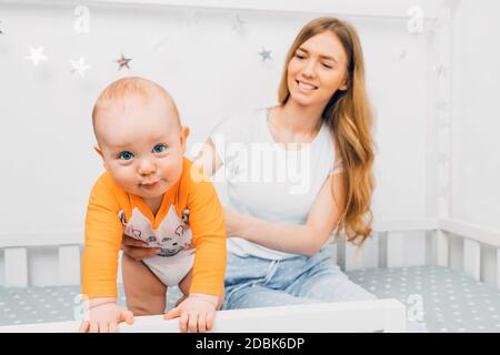 beautiful mother, holding a little boy in her arms, sitting on a child's bed, mom woke up with a baby, children's room Stock Photo