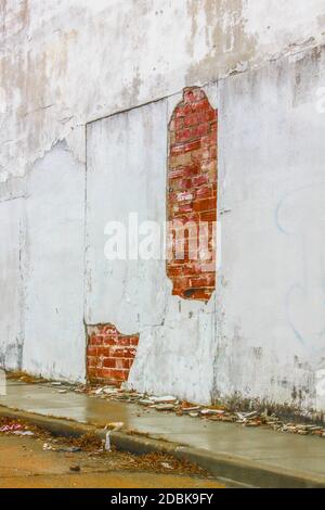 Crumbling wall on rainy day - plaster cracking off exterior building wall and laying in piles on wet grungy sidewalk below - strangely beautiful Stock Photo