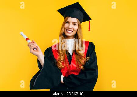 Happy attractive graduate in a master's dress, with a diploma on a yellow  background. Concept of the graduation ceremony Stock Photo - Alamy