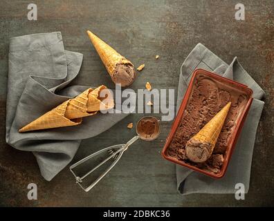 Chocolate ice cream scoops, scooped out of container in to waffle cones with a silver utensil Stock Photo