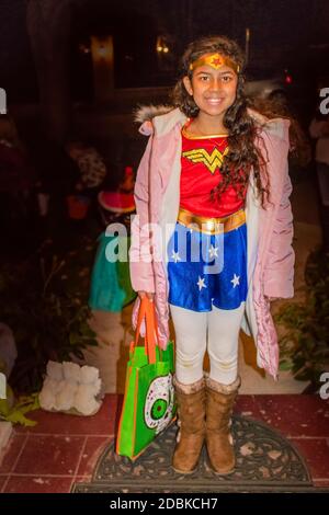 10-31-2017 Beautiful little girl dressed in Wonder Woman costume and a pink coat waits for candy on Halloween Stock Photo