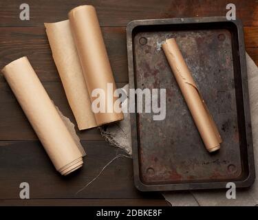 empty rectangular metal pan and rolls of brown parchment paper on a wooden table, top view Stock Photo