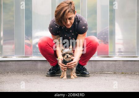Crouched woman holding her yorkshire terrier puppy outdoors Stock Photo