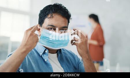 Indian Man Puts on Medical Mask Isolated. Man In Blue Shirt Showing How to put on Medical Mask. Man Puts on Medical Mask in Creative Office. Health Stock Photo