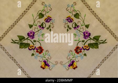 Frame embroidered with bouquets of brown and purple pansies, small blue flowers on curved branches with green leaves Stock Photo