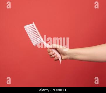 female hand holds pink plastic cleaning brush, red background Stock Photo