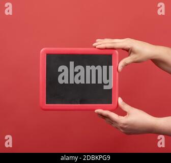 two hands are holding an empty frame on a red background, place for an inscription Stock Photo