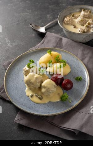 Koenigsberger Klopse or boiled meatballs in a white bechamel sauce with capers, potatoes and beetroot on a blue plate, dark gray background with napki Stock Photo